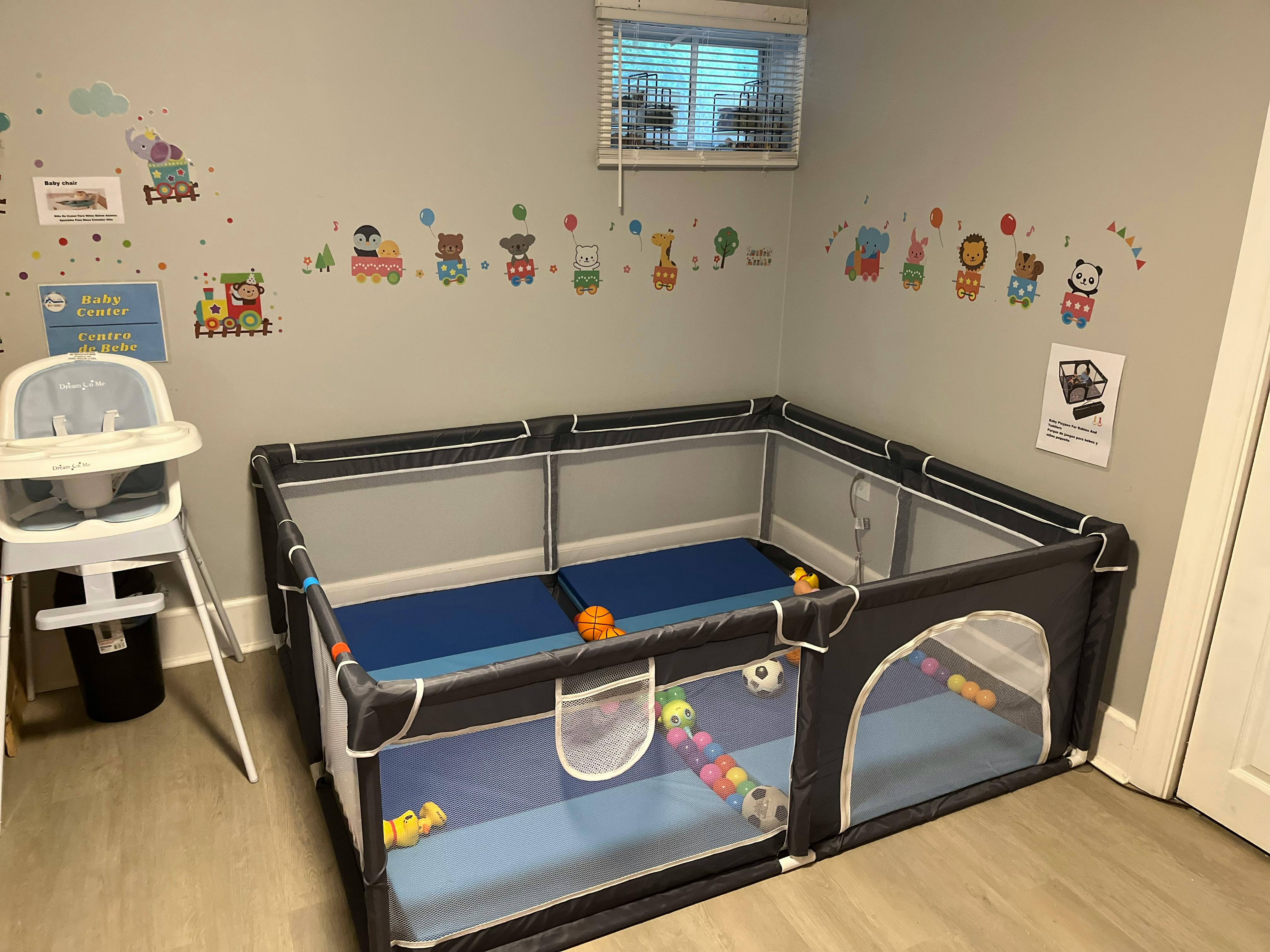 Baby playpen with a high chair next to it, wall decals of animals and trains