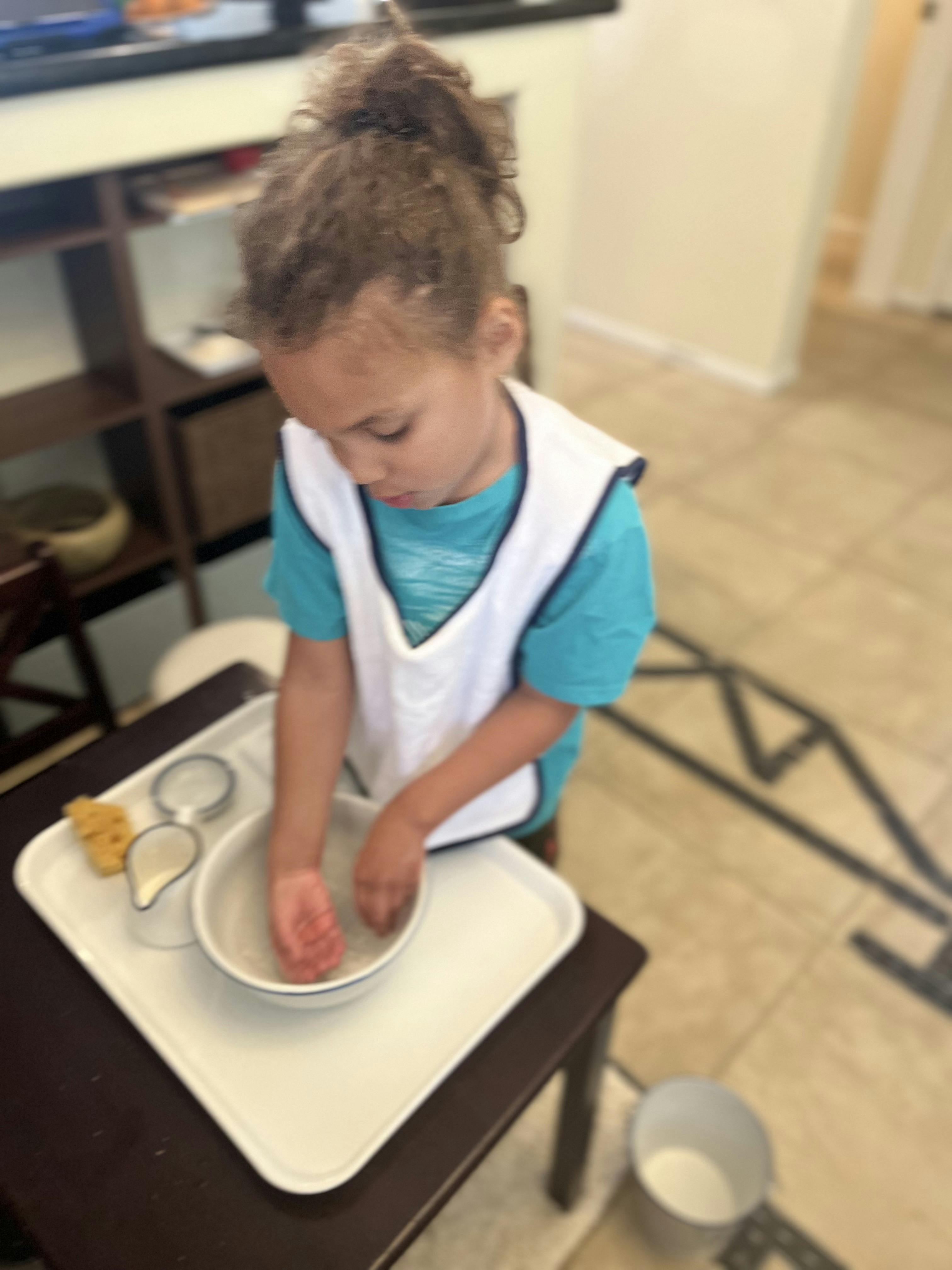 Child wearing an apron, with hands in a bowl