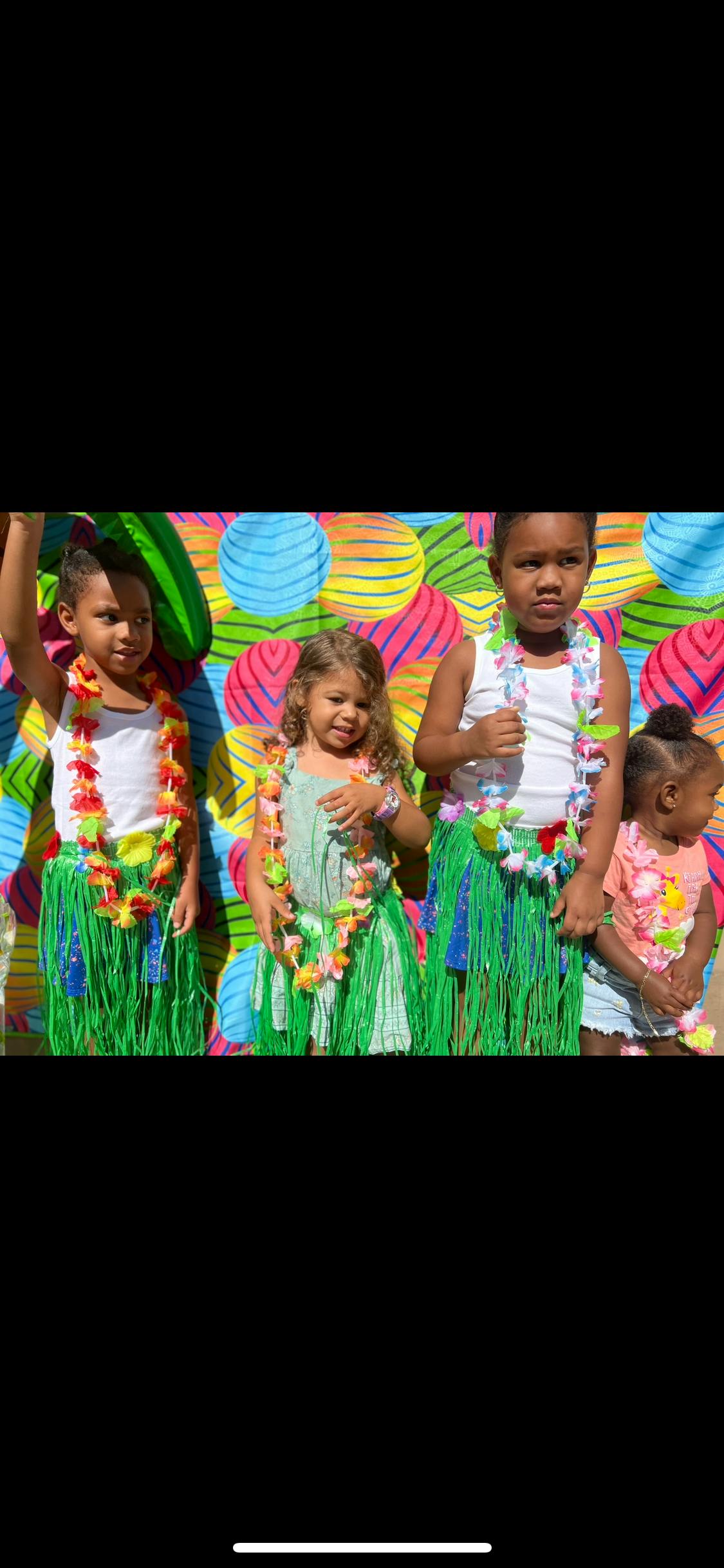 Four children wearing leis and grass skirts