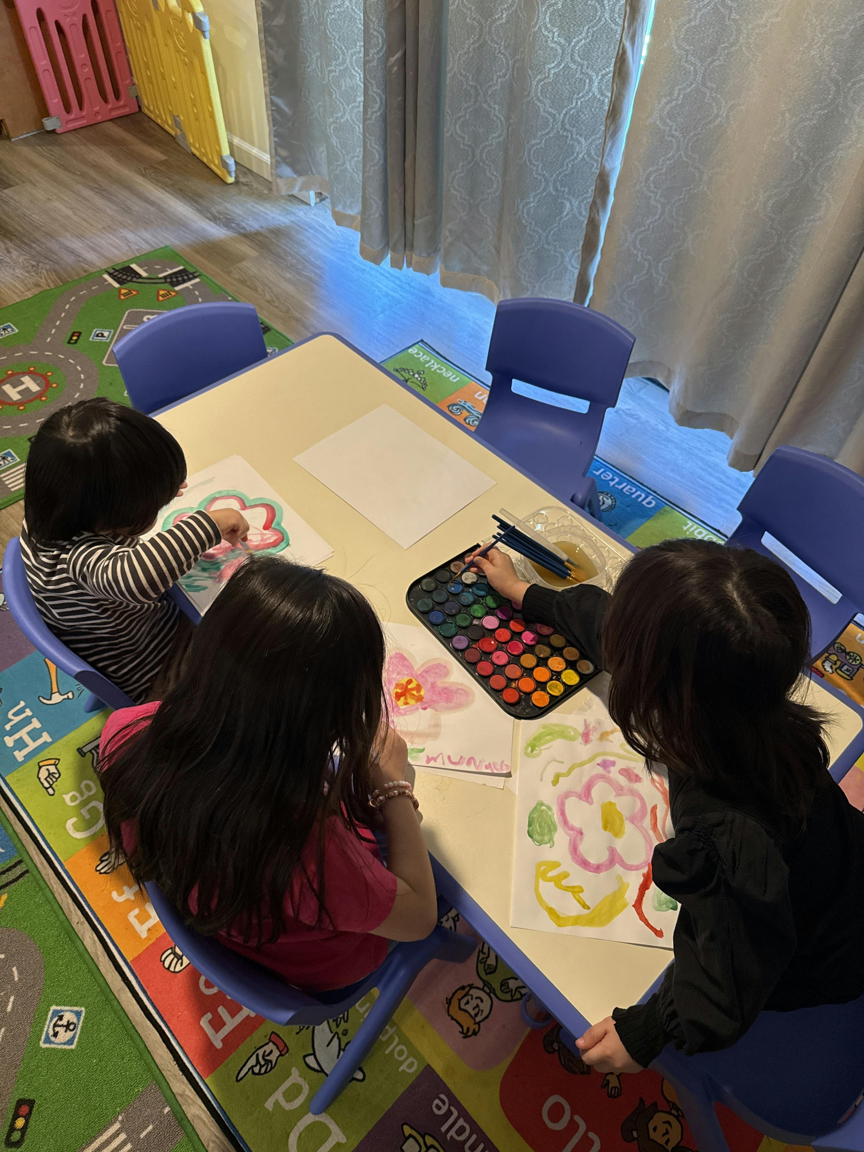 Three children sitting at a table painting with watercolors