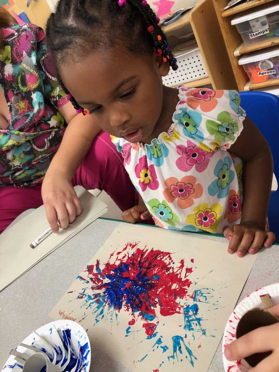Child looking at a painting with red and blue paint splatters