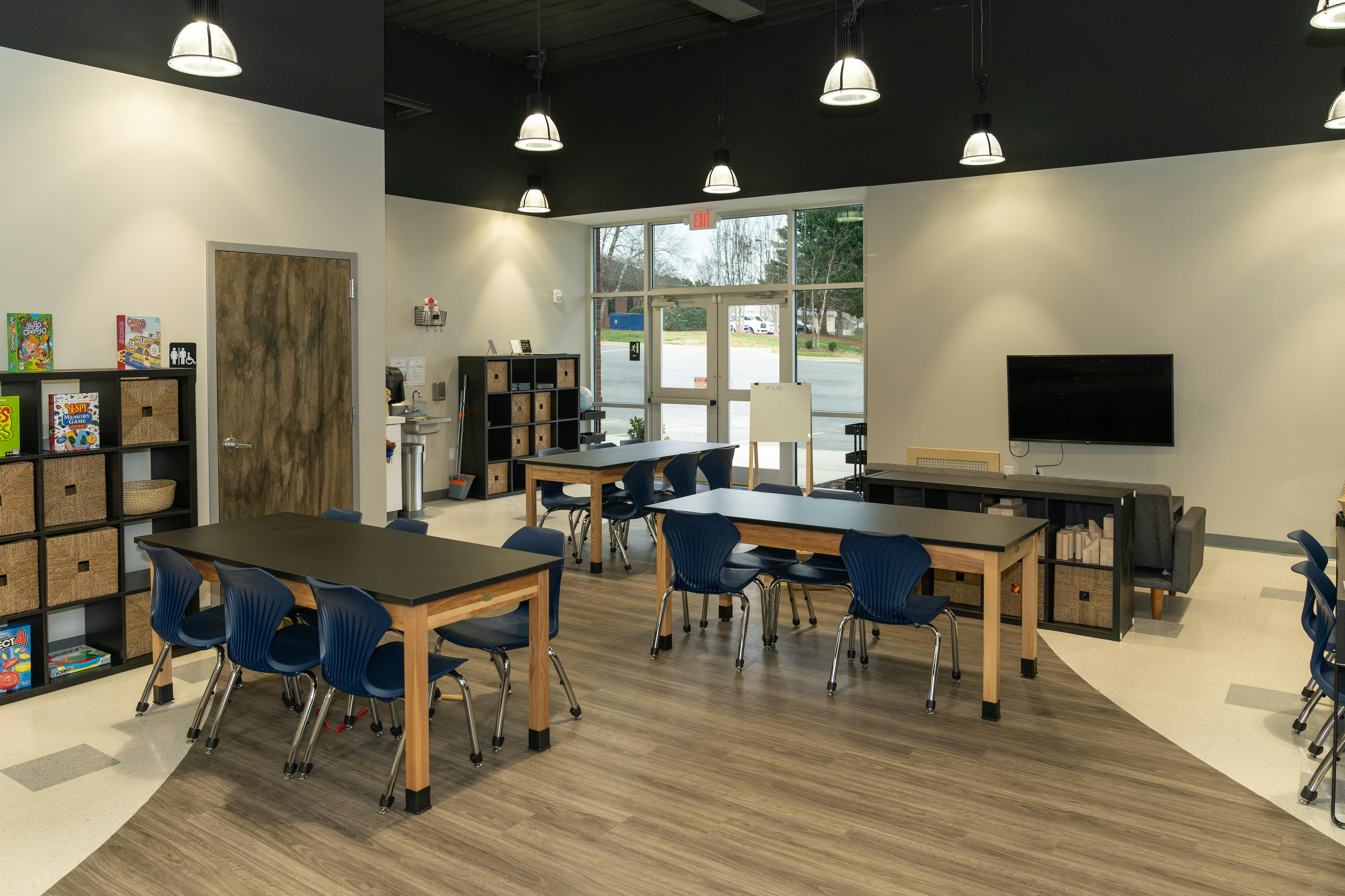Classroom with multiple tables and chairs, shelves, and a television