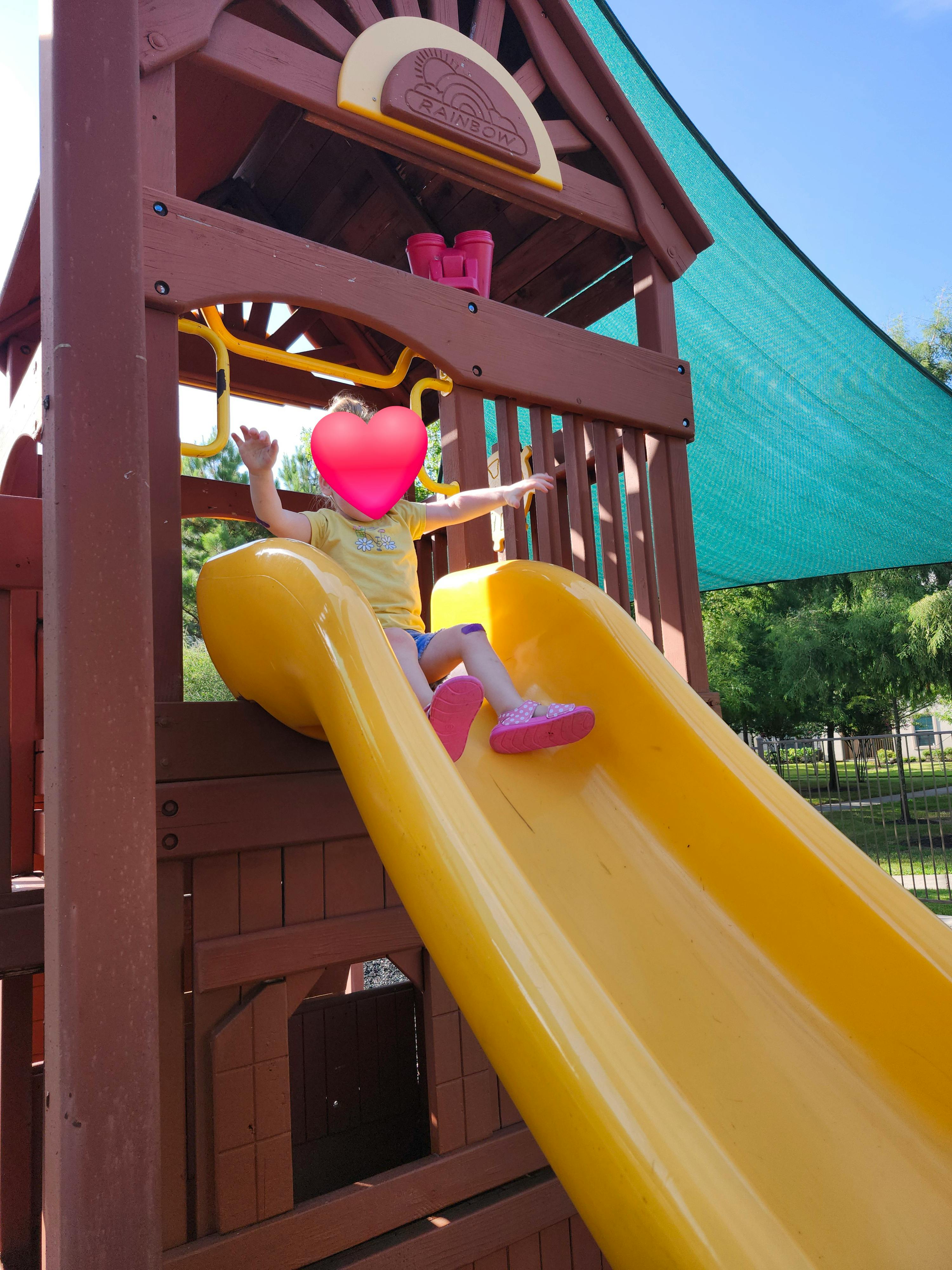 Child sliding down a yellow slide on a playground