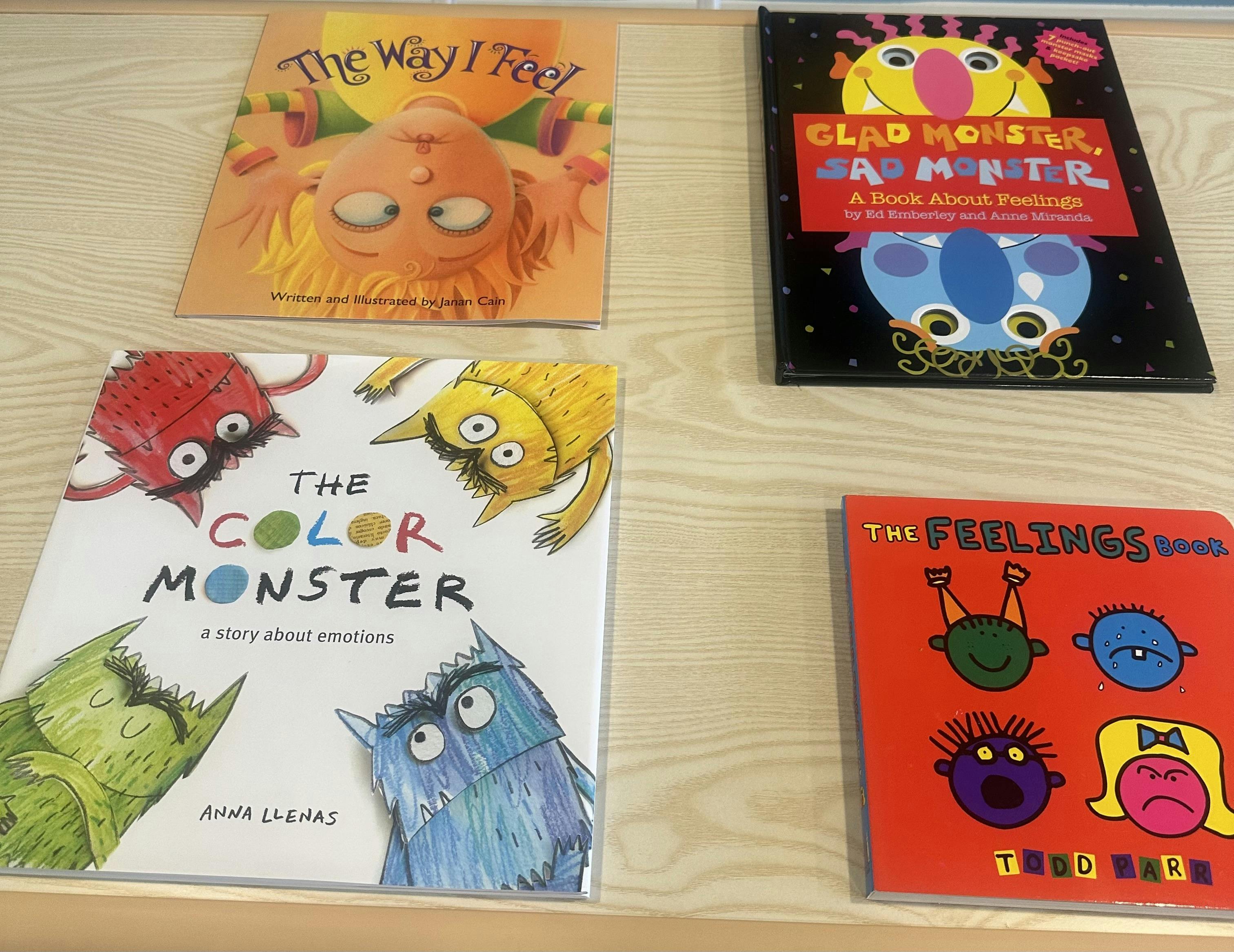 Four children's picture books about feelings arranged on a light wooden table
