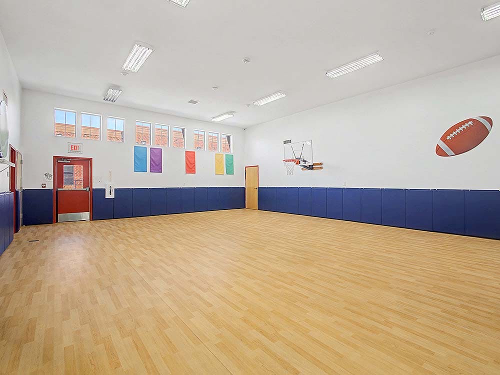 Empty gymnasium with hardwood floor, exit sign above red door