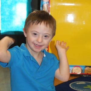 Child with Down syndrome smiling and raising hands