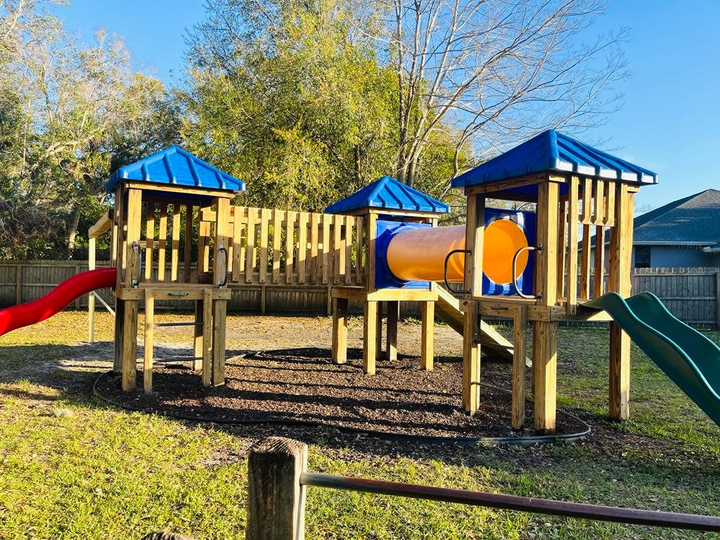 Wooden playground structure with blue roofs, red slide, and green slide