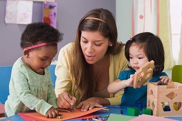 Adult and two children drawing and playing with toys in a classroom