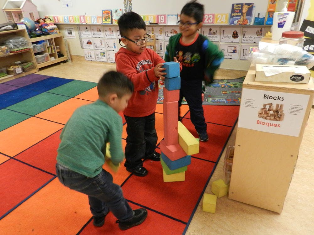 Three children playing with large building blocks in a classroom