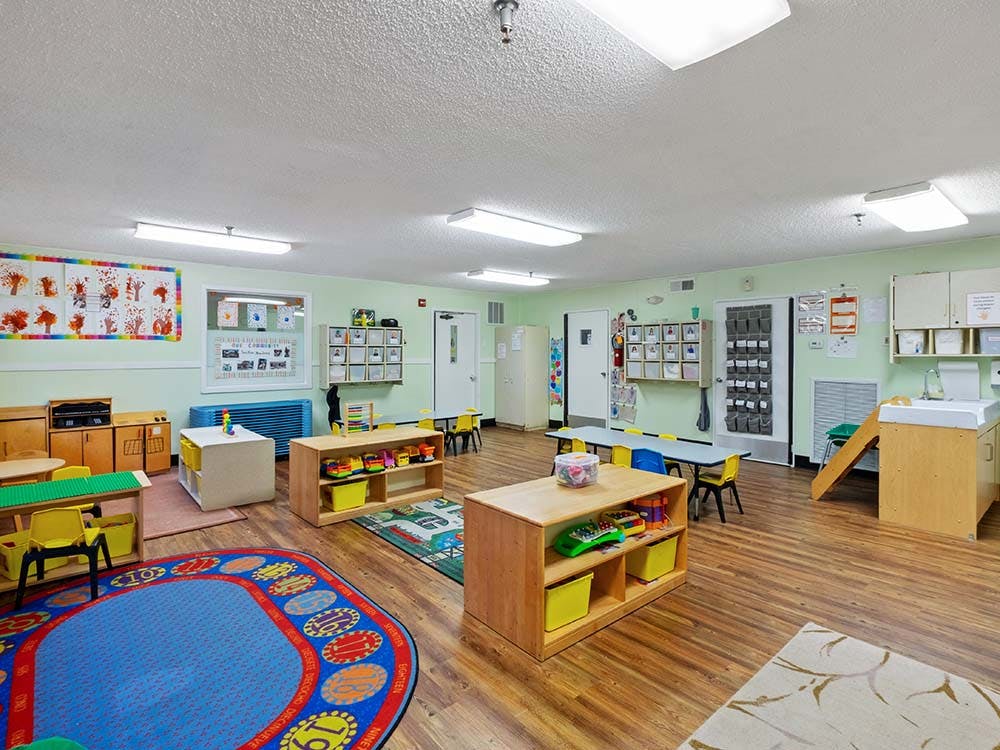 Empty colorful preschool classroom with small tables, chairs, and play equipment