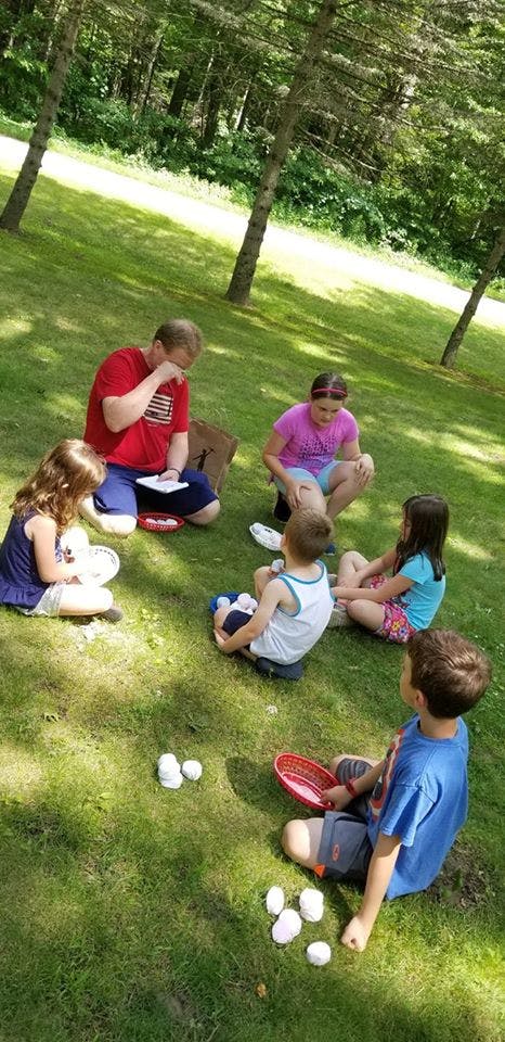 Adult and children sitting on grass with small white objects
