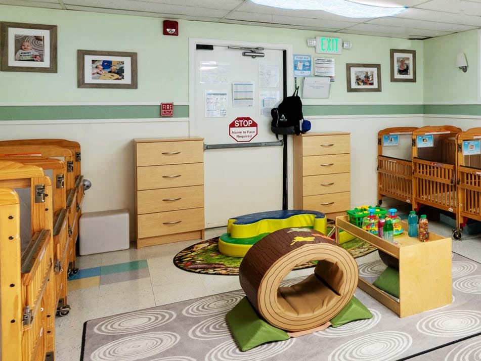 Empty infant room with cribs, drawers, and soft play equipment