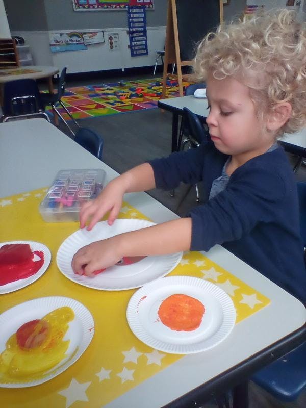 Child finger painting at a table in a classroom