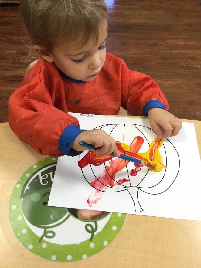 Child painting a pumpkin outline with red and yellow paint