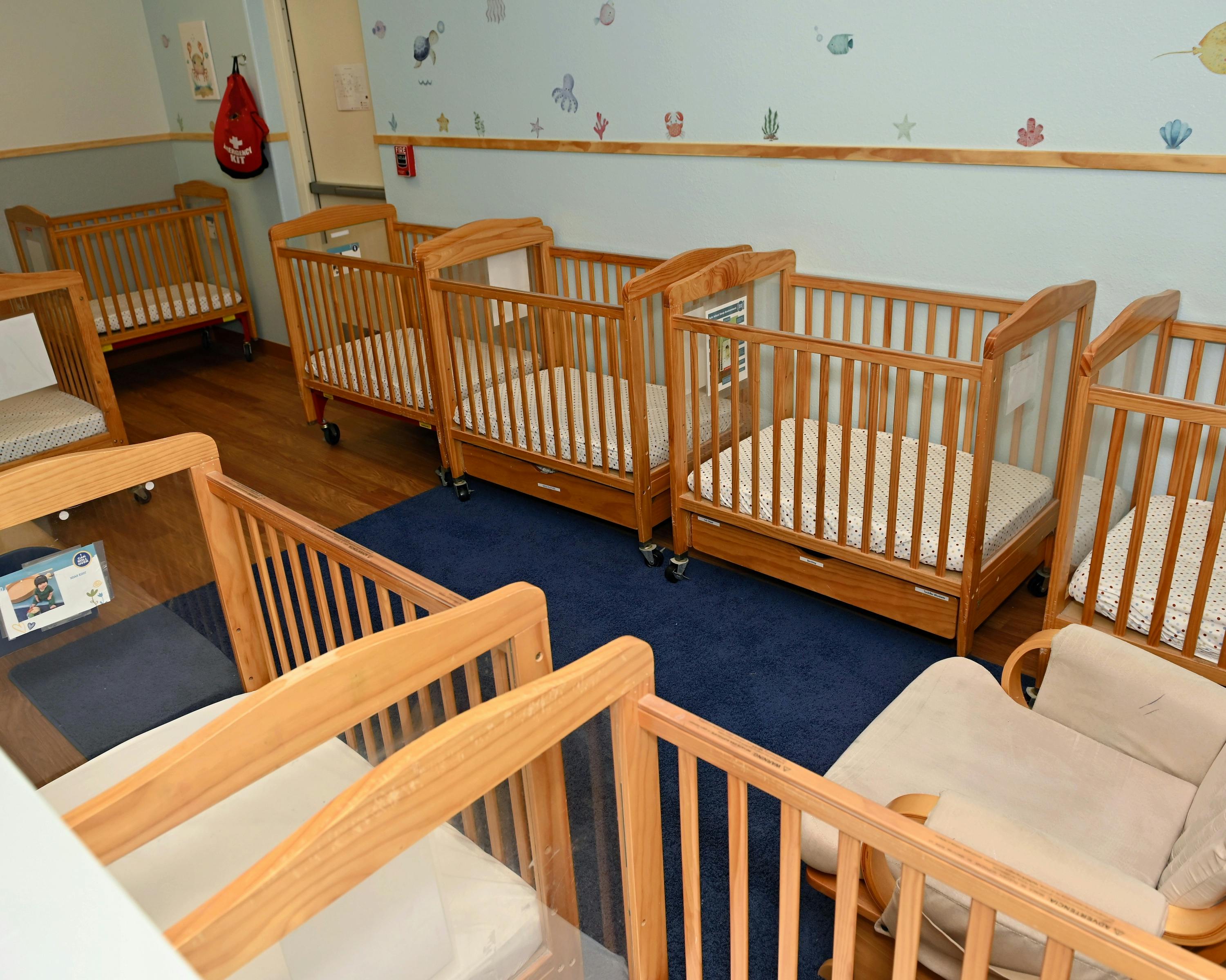 multiple wooden cribs with mattresses in a nursery room with a blue wall