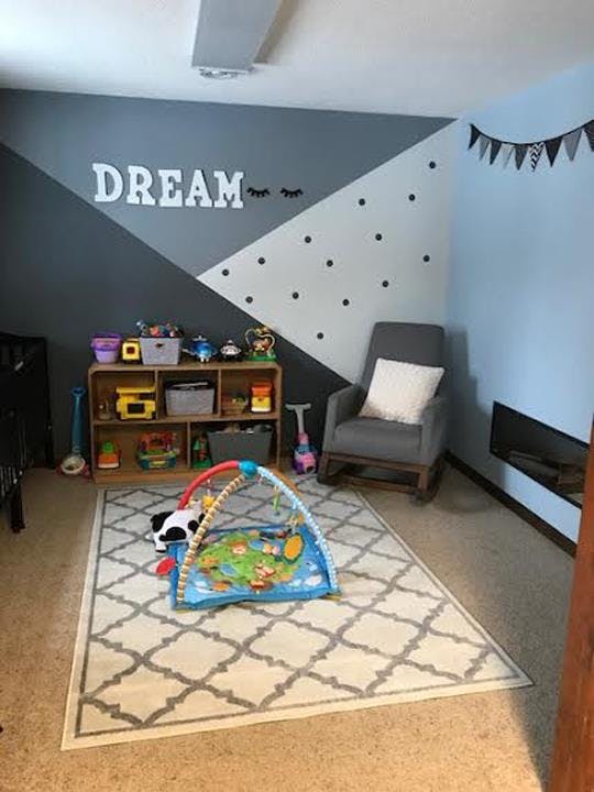 Nursery room with a play mat on a rug, a bookshelf with toys, and a rocking chair