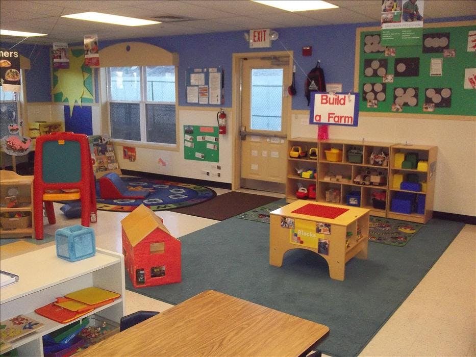 A colorful empty classroom with toys, a rug, tables, and a sign that says "Build a Farm"