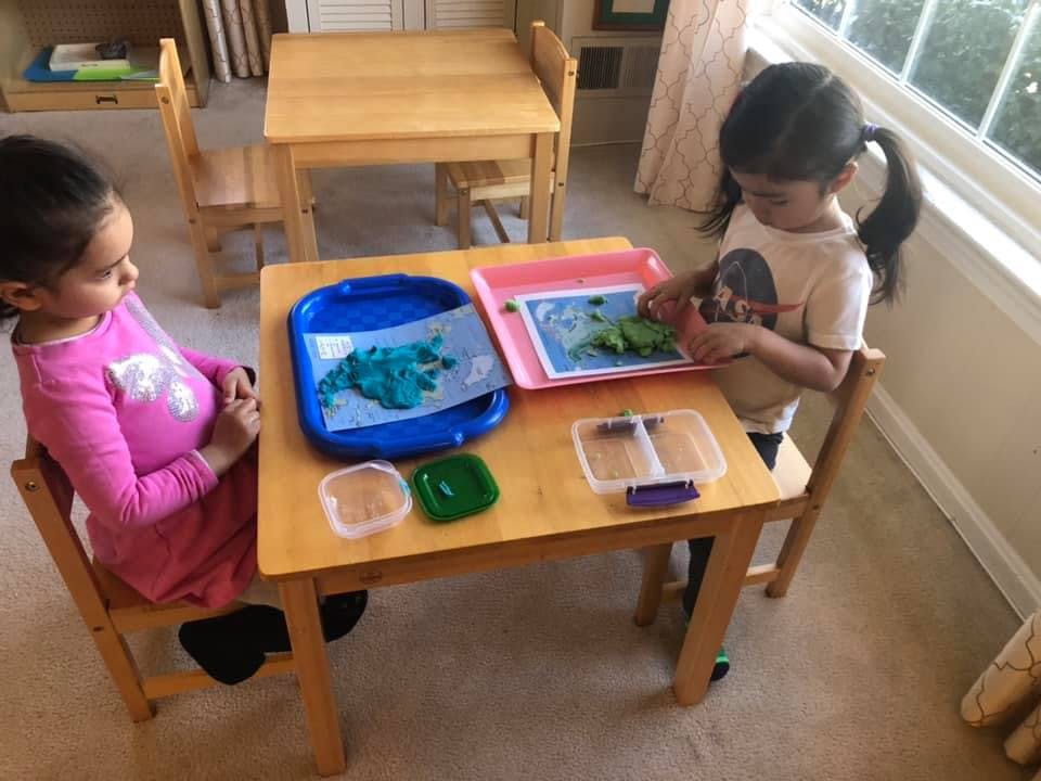 Two children at a table, one playing with modeling clay
