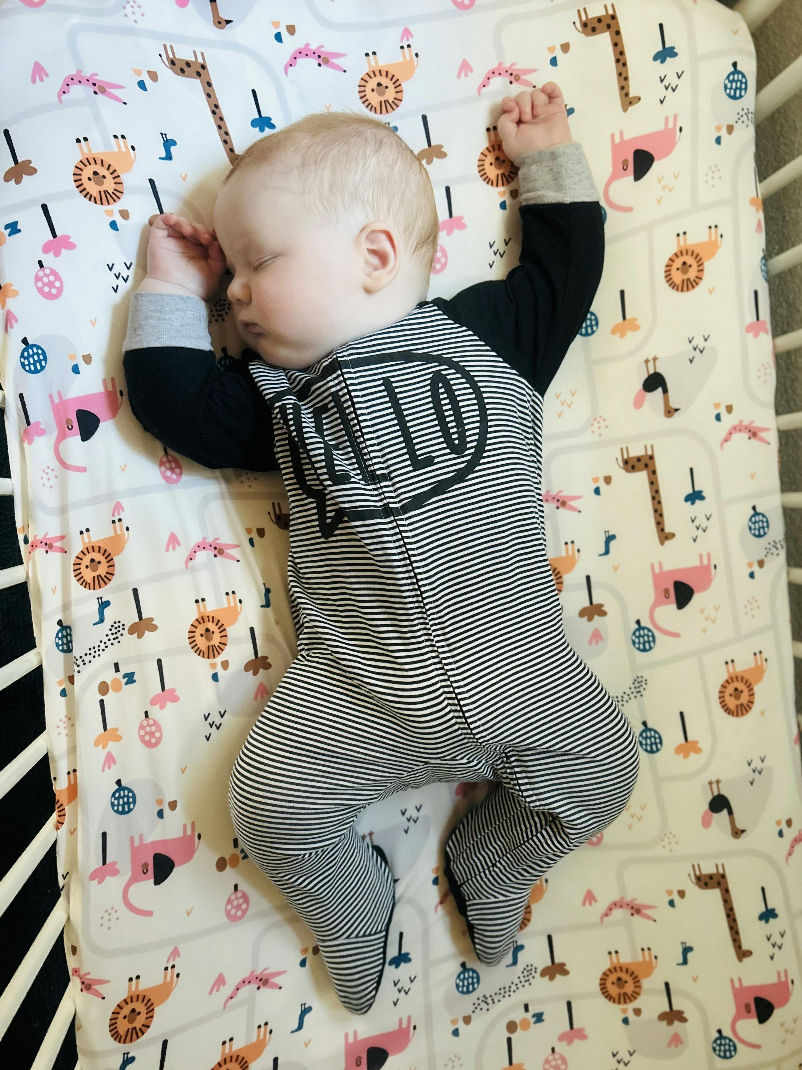 Sleeping baby in a crib wearing a striped onesie with "HELLO" written on it