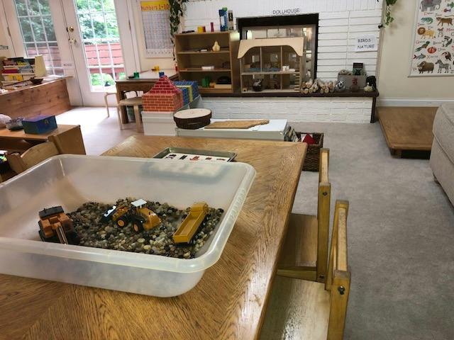 Plastic bin with toy construction vehicles and gravel on a table in a classroom