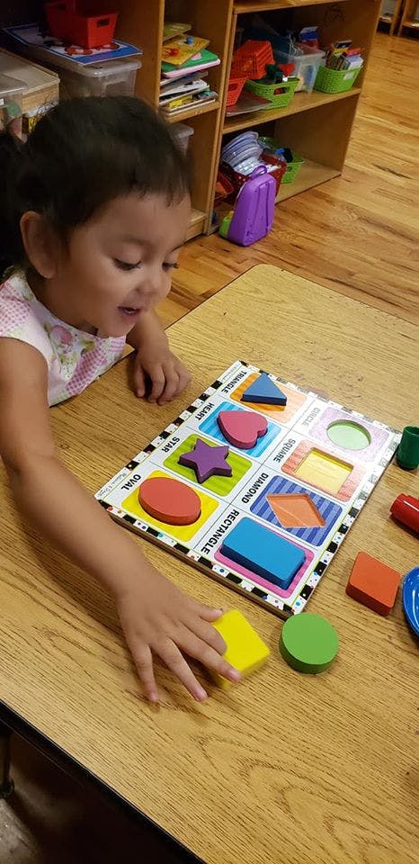 Child playing with a shape sorter puzzle on a wooden table