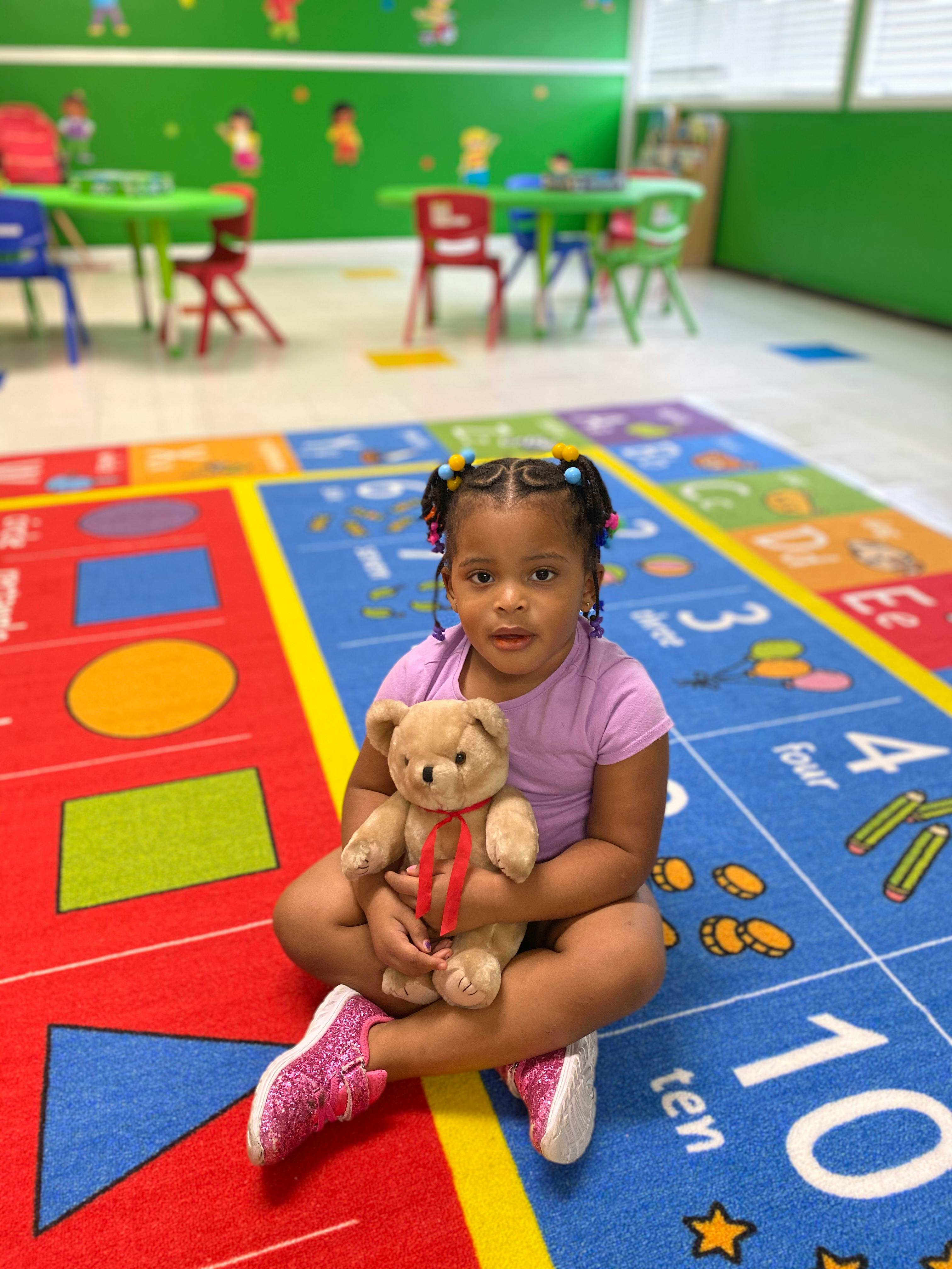 Child sitting on a colorful rug holding a teddy bear in a classroom