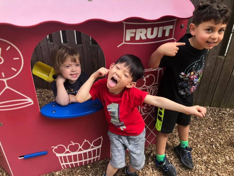 Three children playing in a red playhouse with "FRUIT" written on it