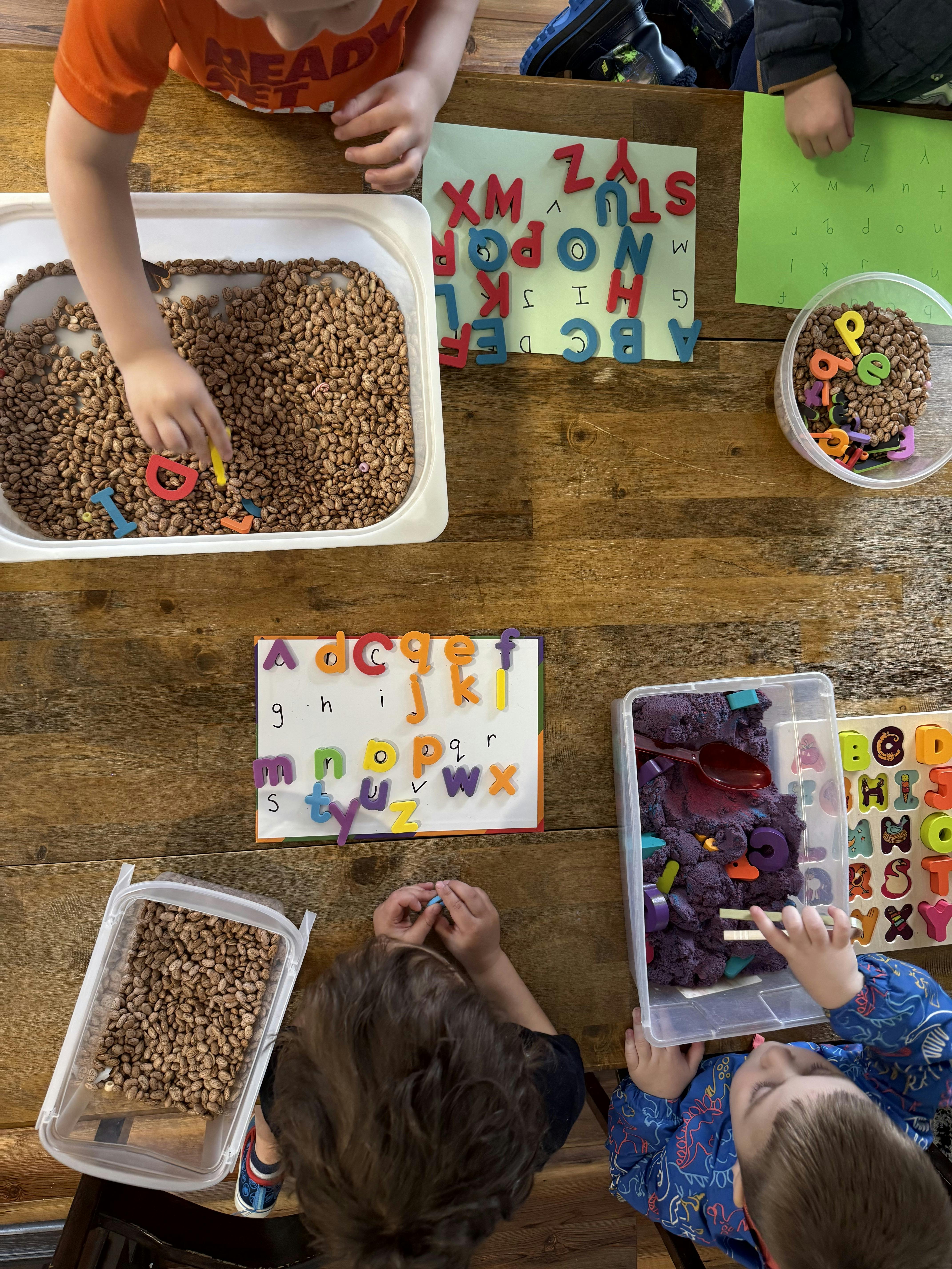 overhead view of children playing with alphabet letters and sensory bins
