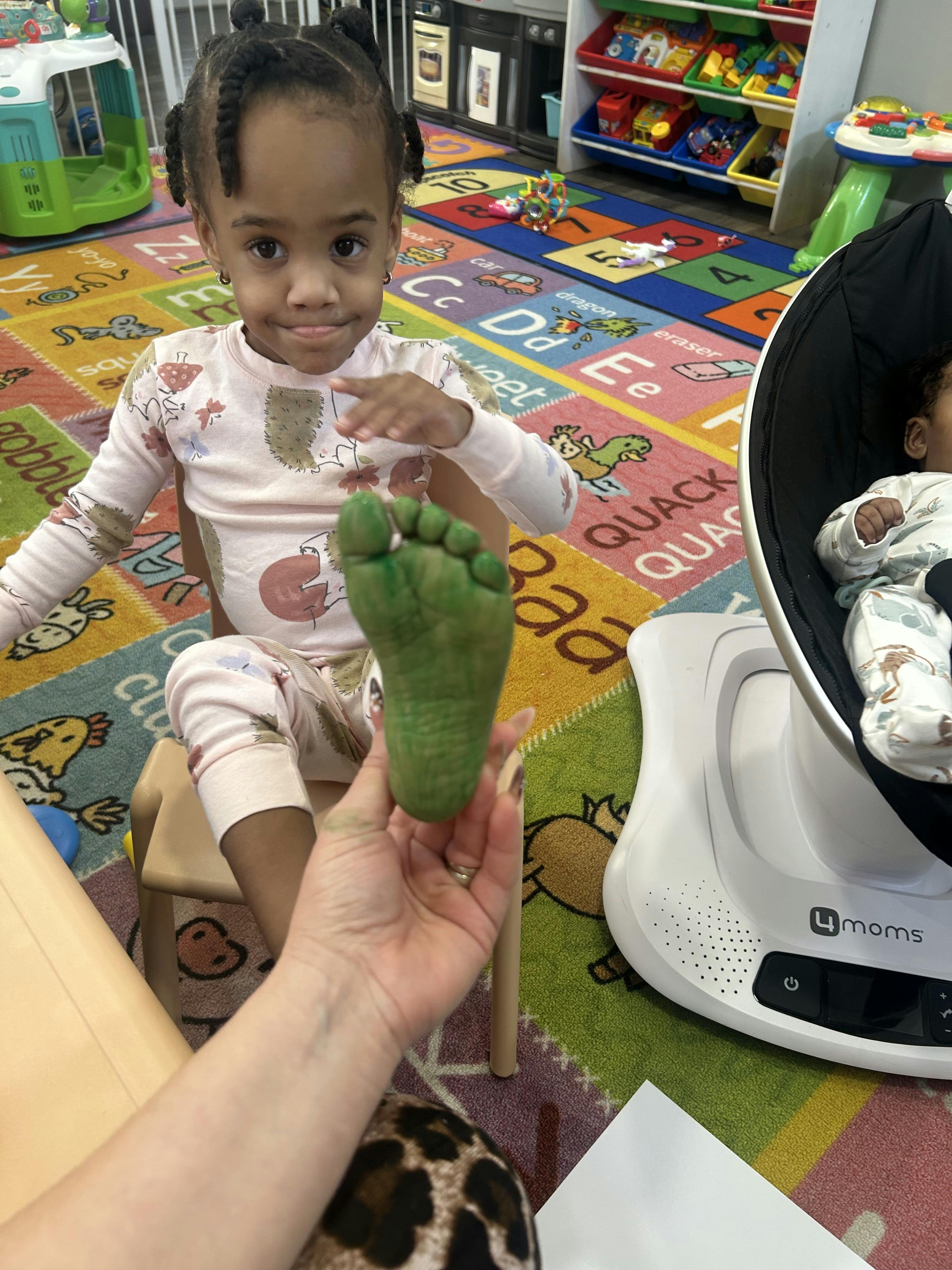 Child sitting in a classroom, looking at a person holding a foot painted green