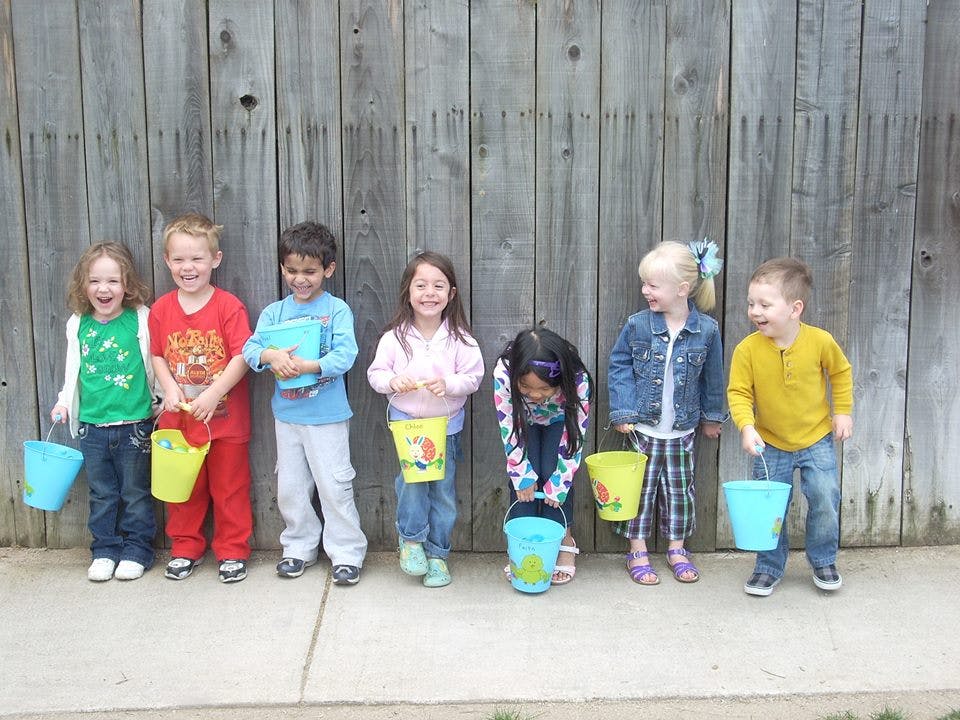 Group of children holding buckets in front of a wooden fence
