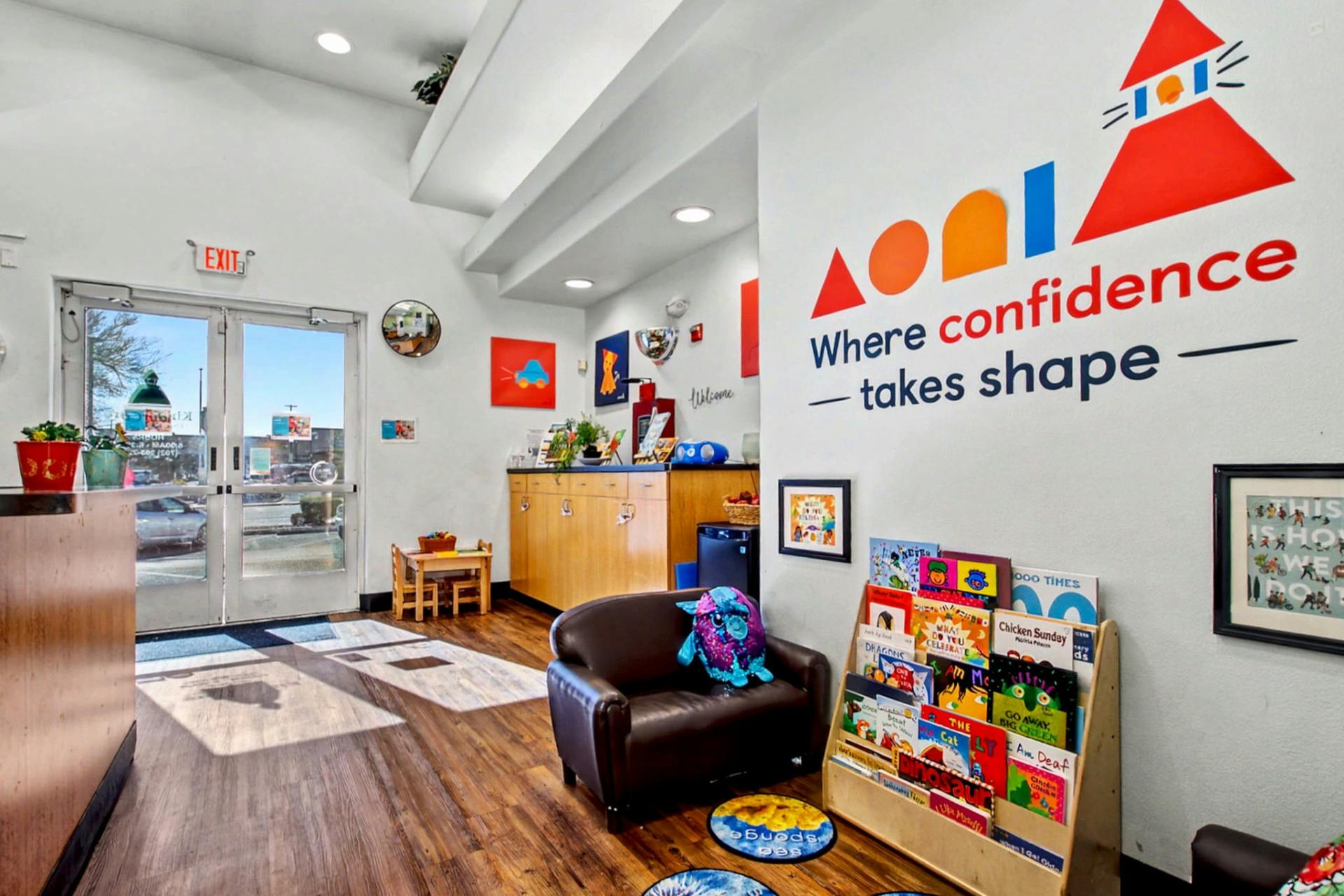 Children's reception area with a bookshelf and a sign that reads 'Where confidence takes shape'