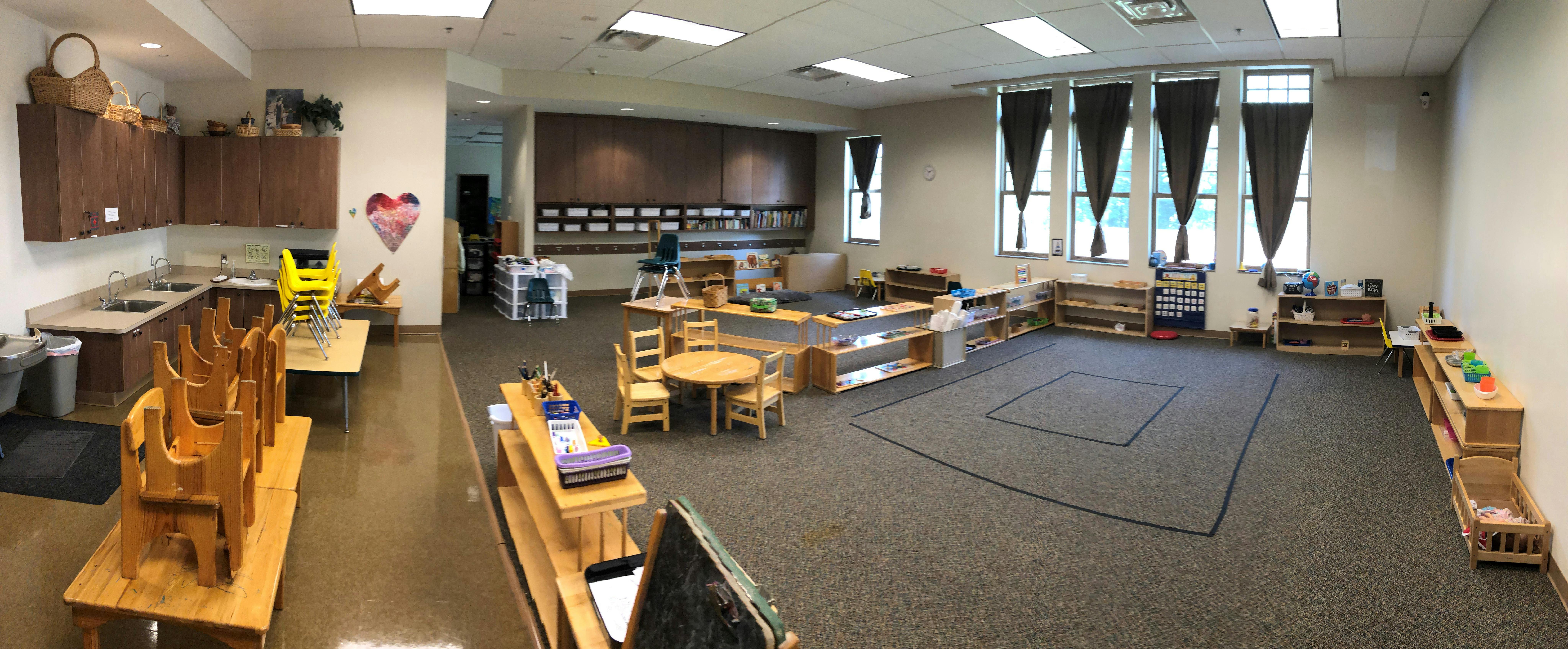 Empty classroom with small tables and chairs, shelves, and a kitchen area