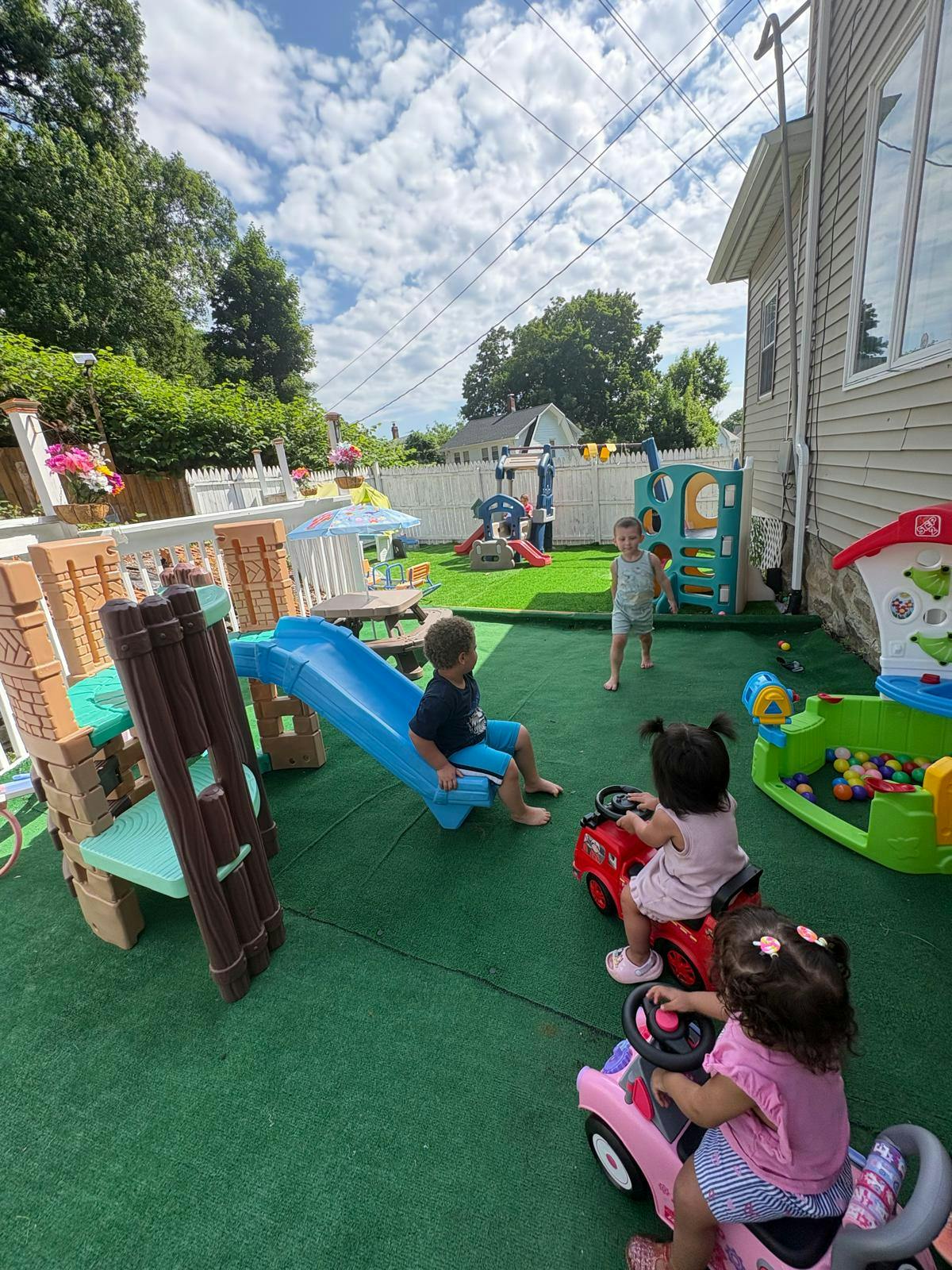 Children playing with toys and a slide on a backyard turf area
