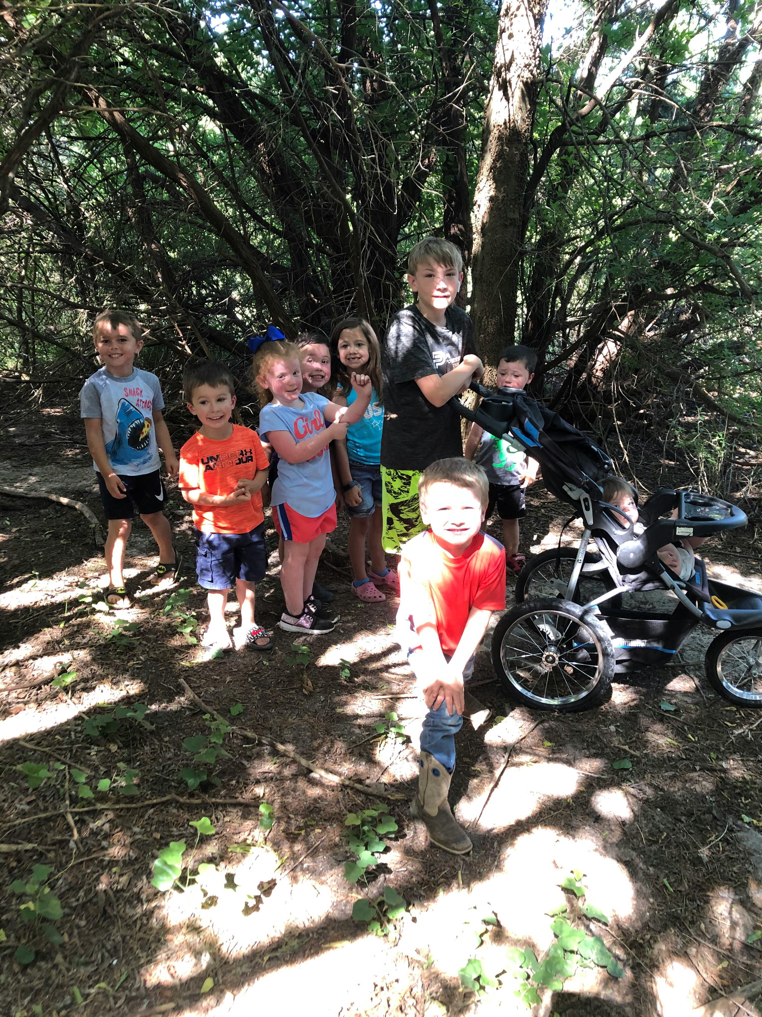 Group of children standing in a wooded area with a stroller