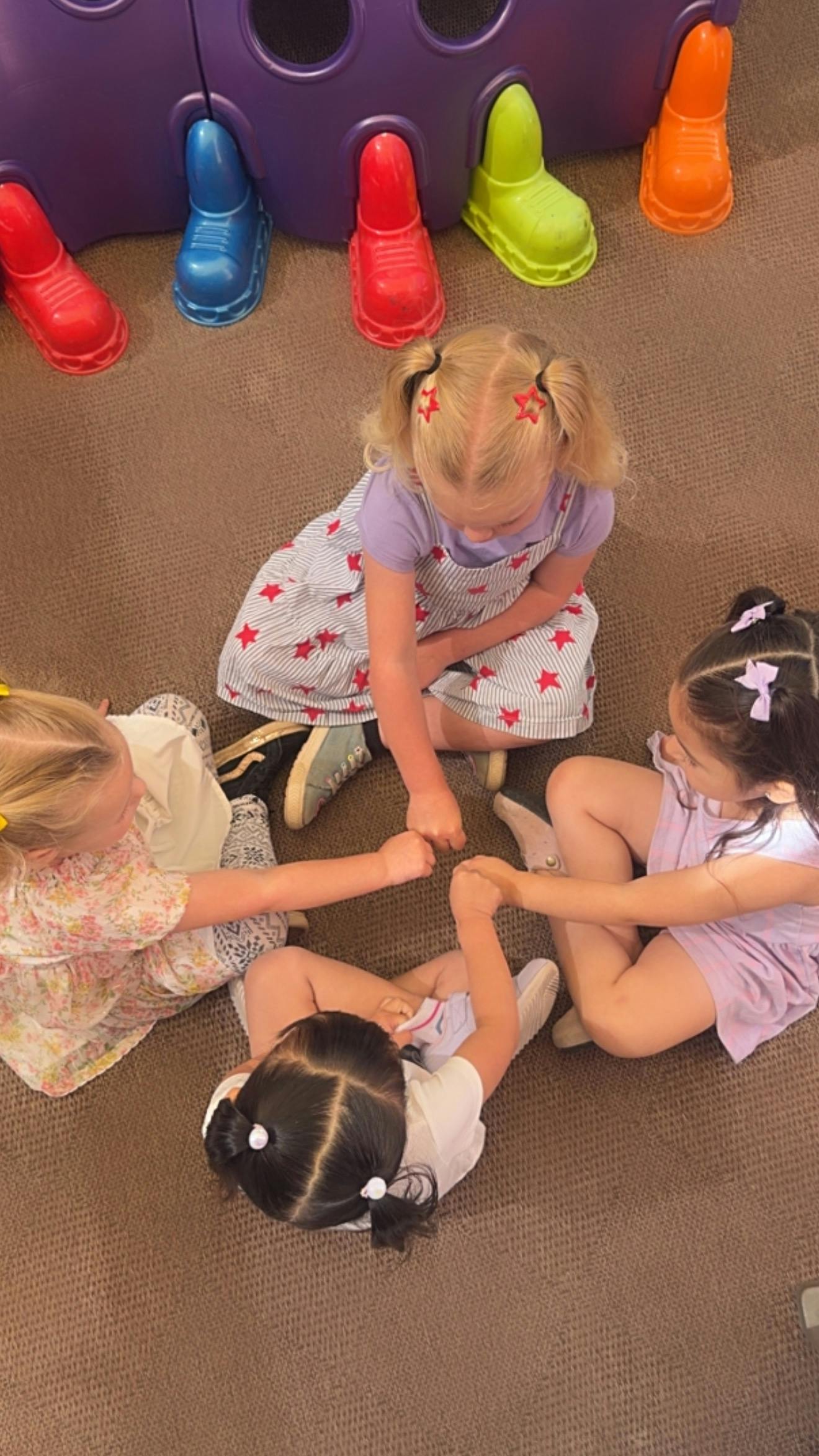 Three children sitting in a circle, holding hands with their fists closed
