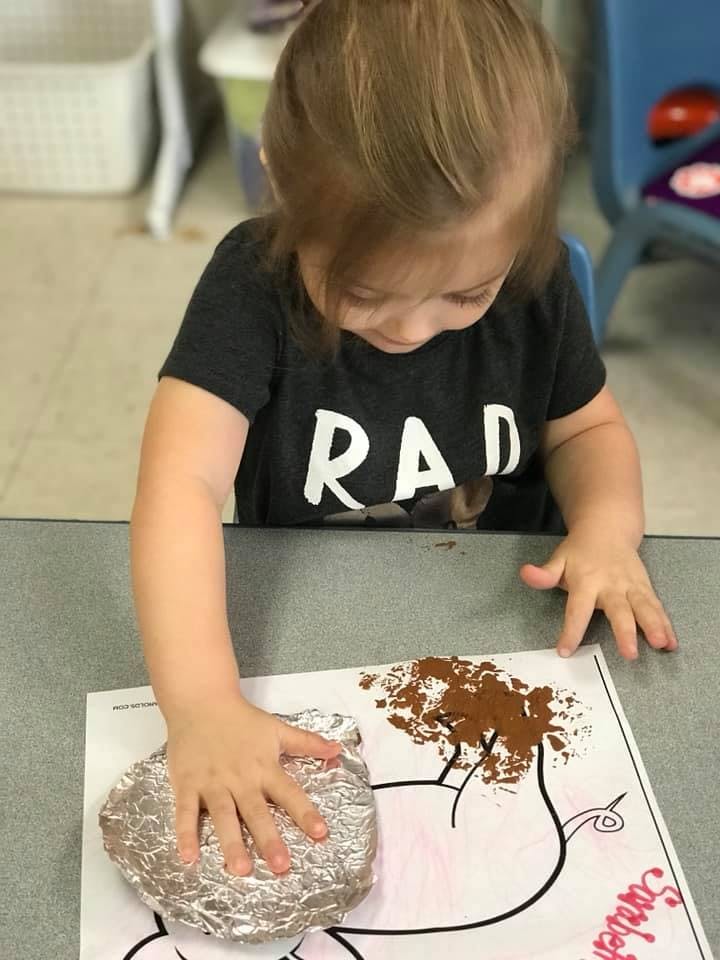 Child pressing foil onto a paper with brown paint
