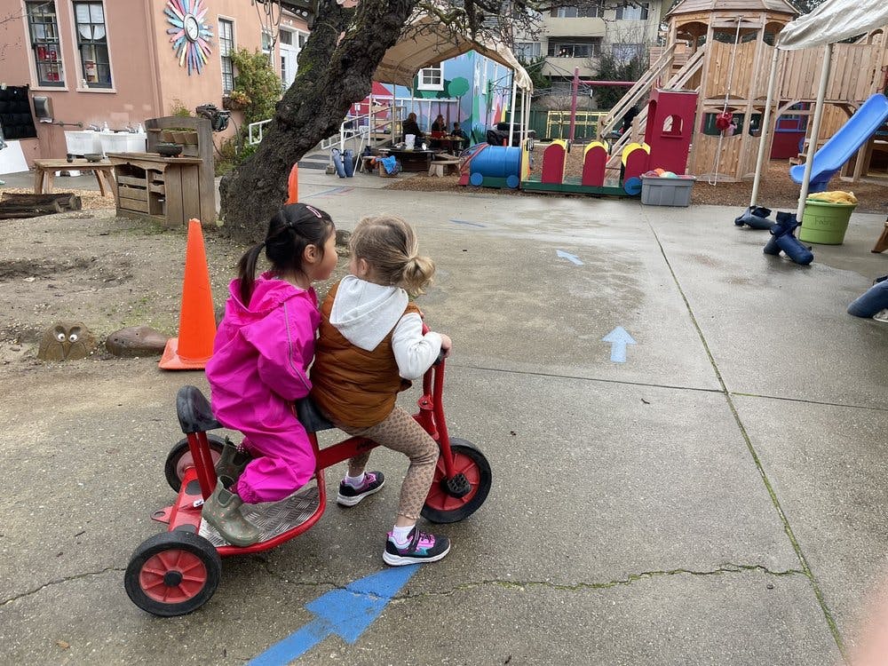 Two children riding a red tricycle on a playground