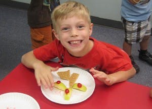 Child smiling at a table with a plate of food