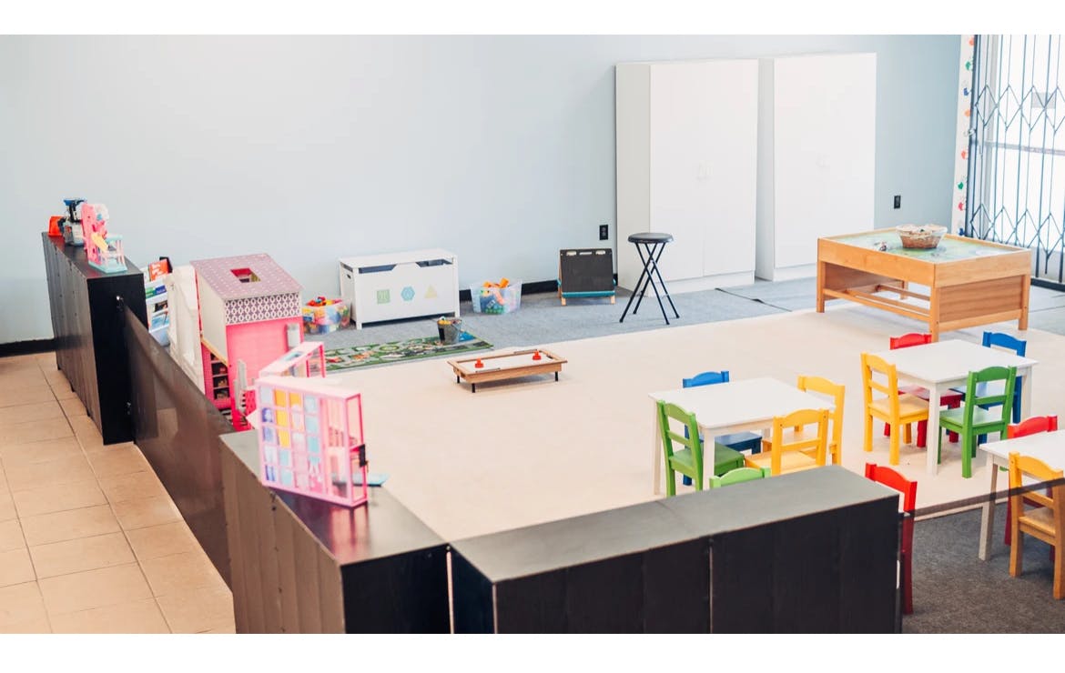 Playroom with small tables and chairs, and toys on the left, a counter with toys