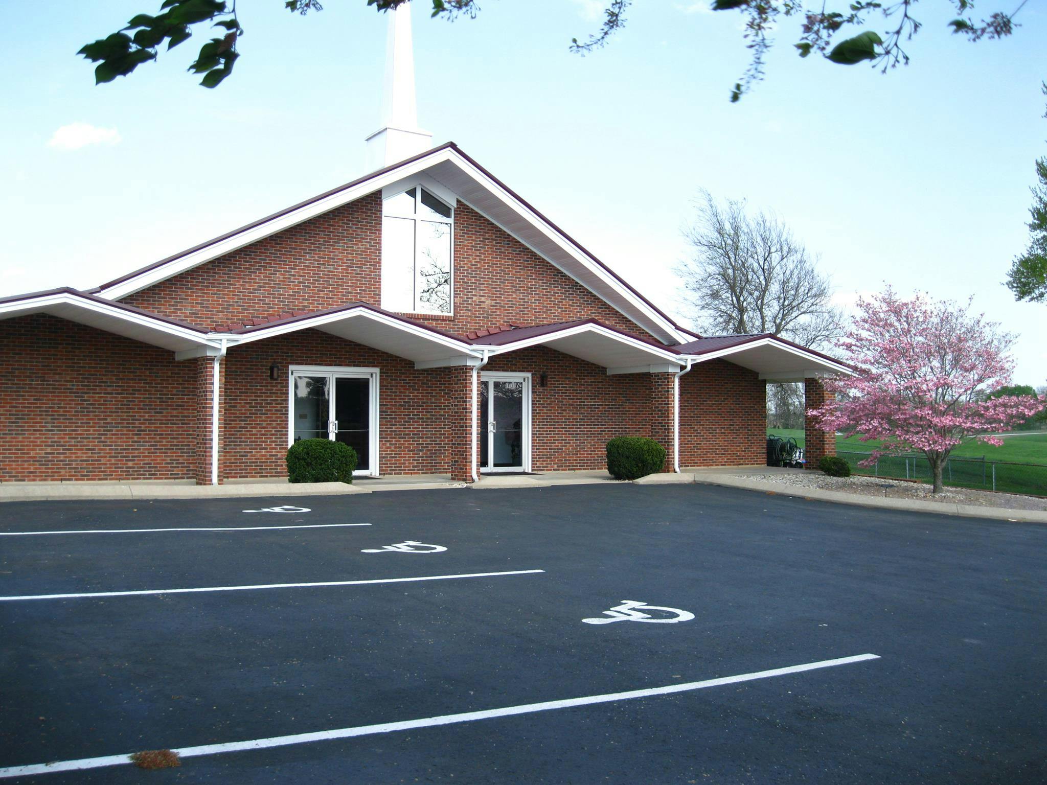 Brick building with a white steeple and a parking lot with handicap spaces