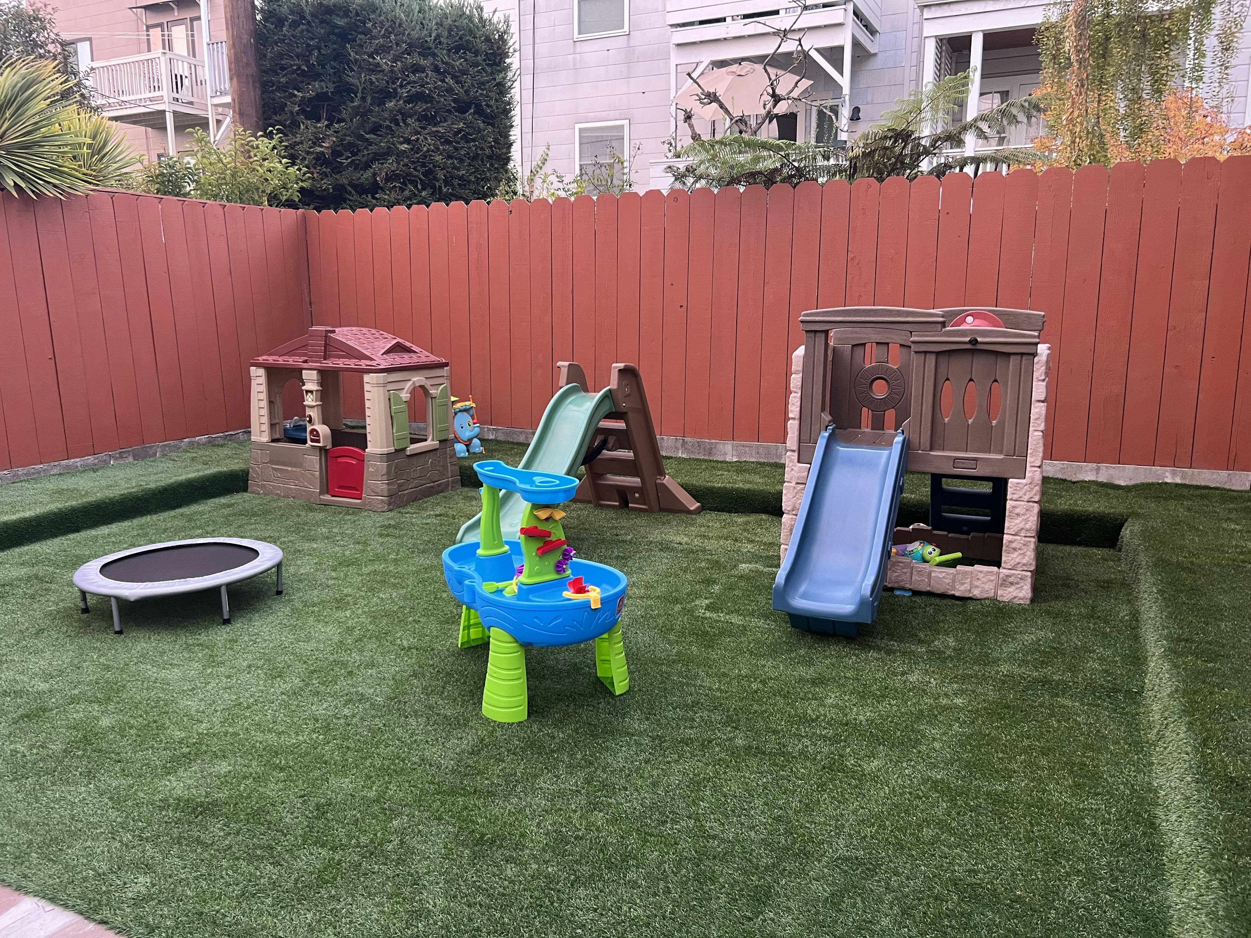 Playground with slides, playhouses, water table, and trampoline on artificial turf