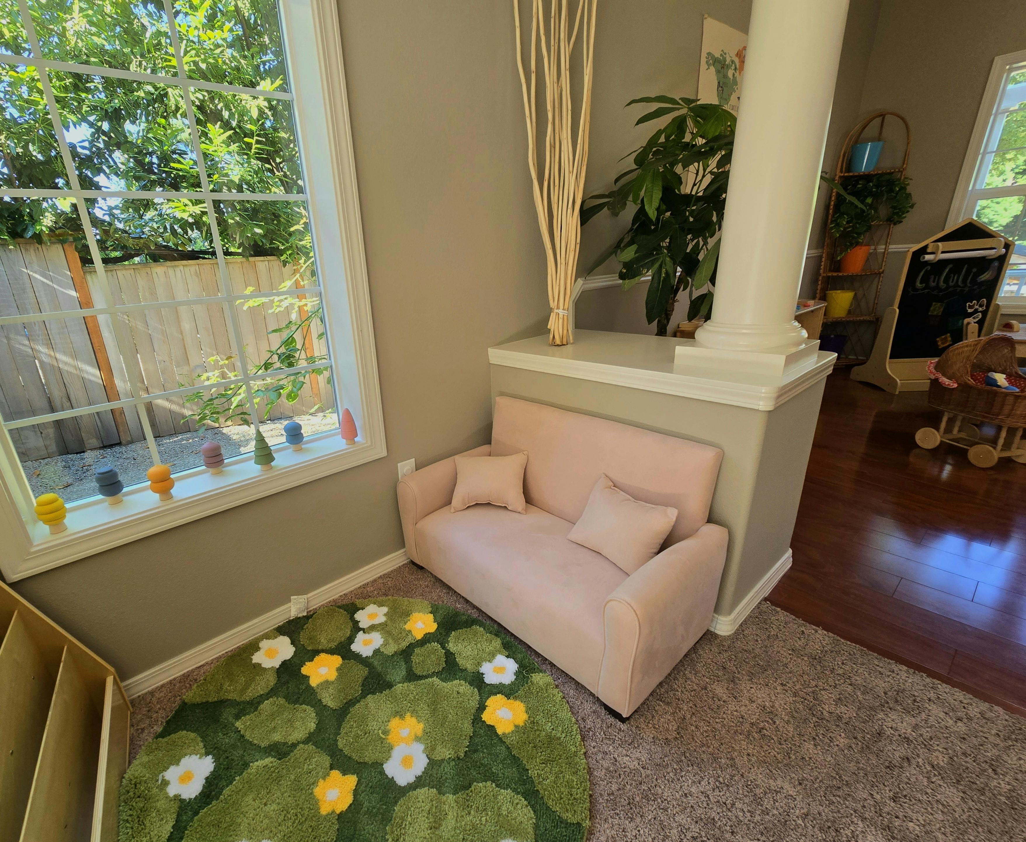 Pink sofa with pillows next to a window and a lily pad rug