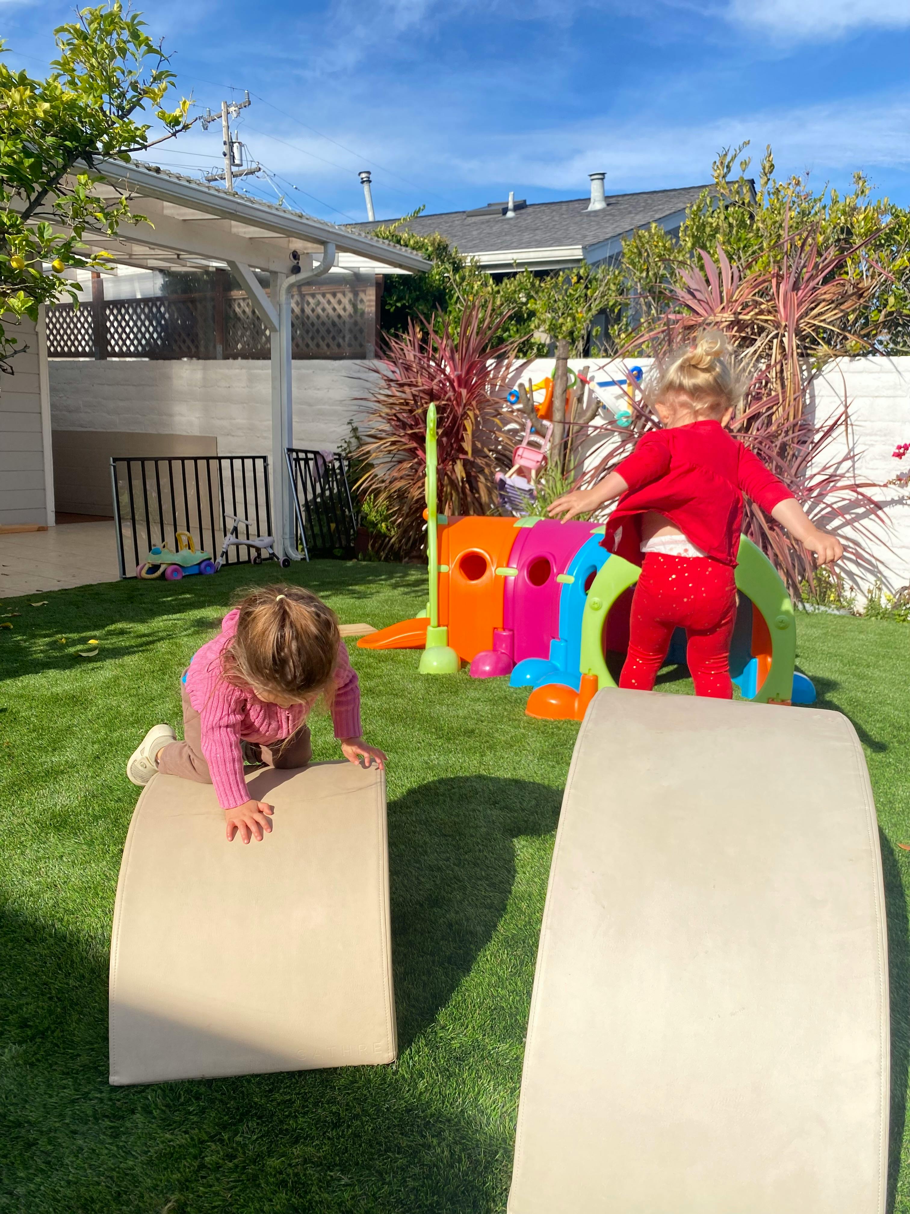 Two children playing on outdoor play equipment in a grassy yard