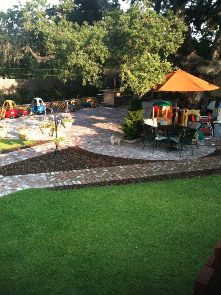 Backyard patio with brick pavers, green lawn, and children's toys