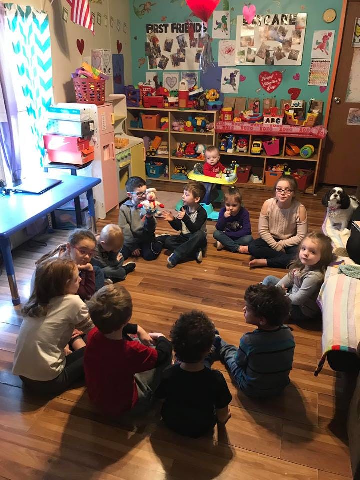 Children and adults sitting in a circle on a wooden floor in a classroom