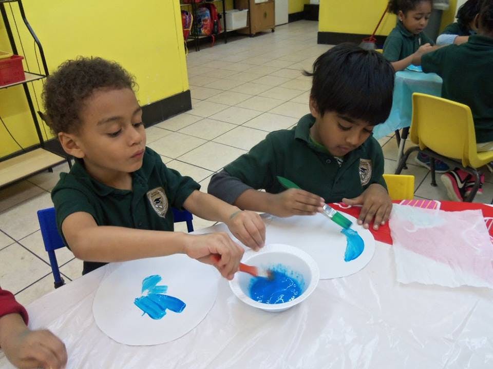 Two children painting with blue paint in a classroom