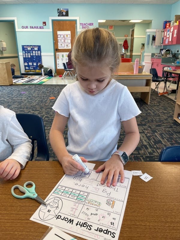 Child gluing paper onto a "Super Sight Word" worksheet in a classroom