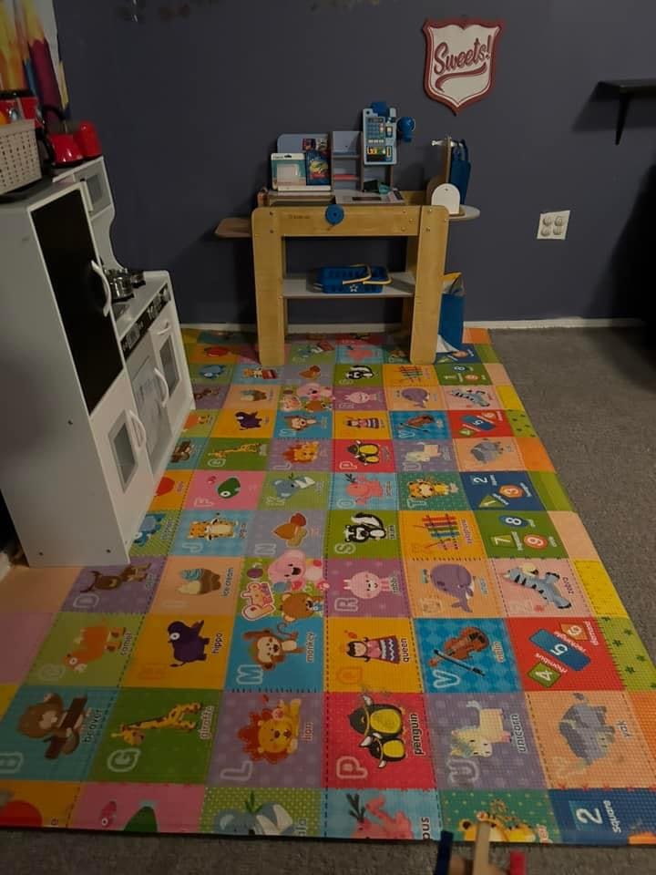 Playroom with a colorful alphabet mat, toy kitchen, and wooden table