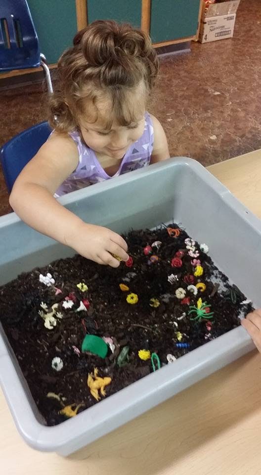 Child playing with a sensory bin filled with dirt and small toys