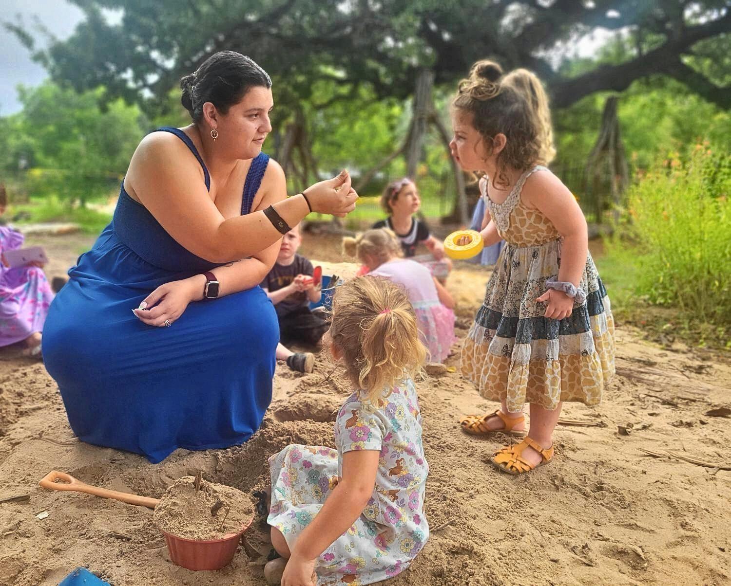 Person in blue dress interacting with children in sand